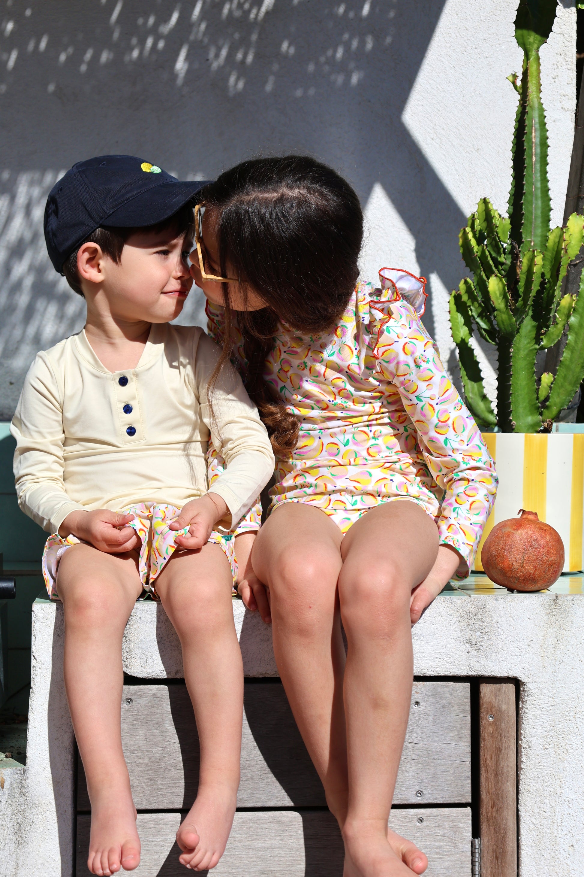 Frère et sœur portant l'ensemble anti-UV Smoothie Loumio Paris, s'échangeant un bisou sous le soleil.