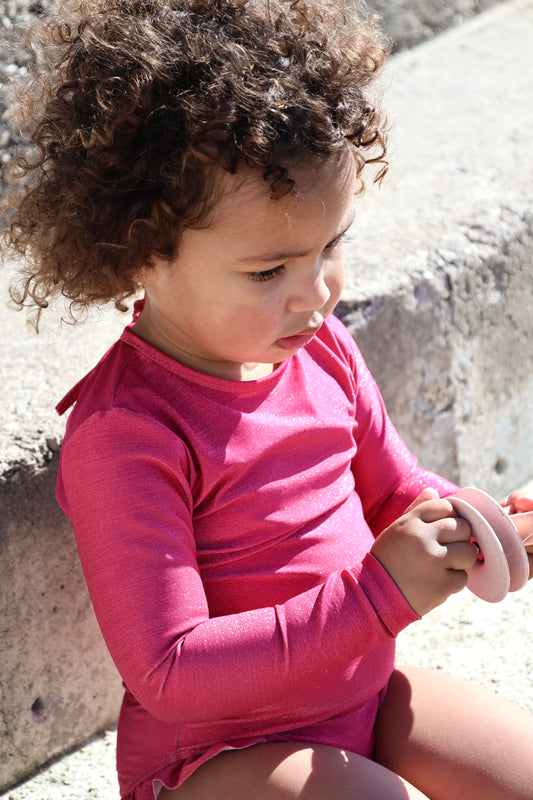 petite fille portant un maillot de bain une pièce manches longues Alba framboise de Loumio Paris sur la plage