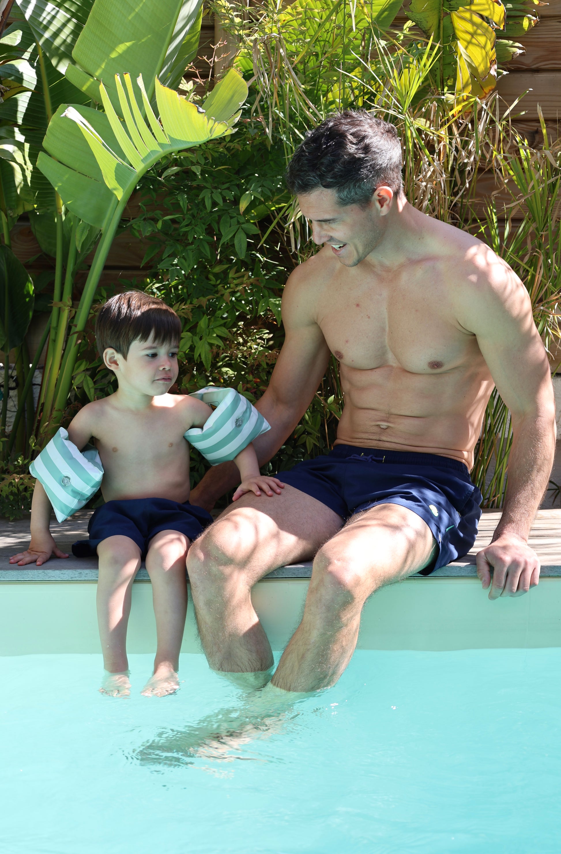 Père et fils portant le short de bain Orso Deep Blue Loumio Paris à la piscine, prêts à profiter de l'eau et du soleil