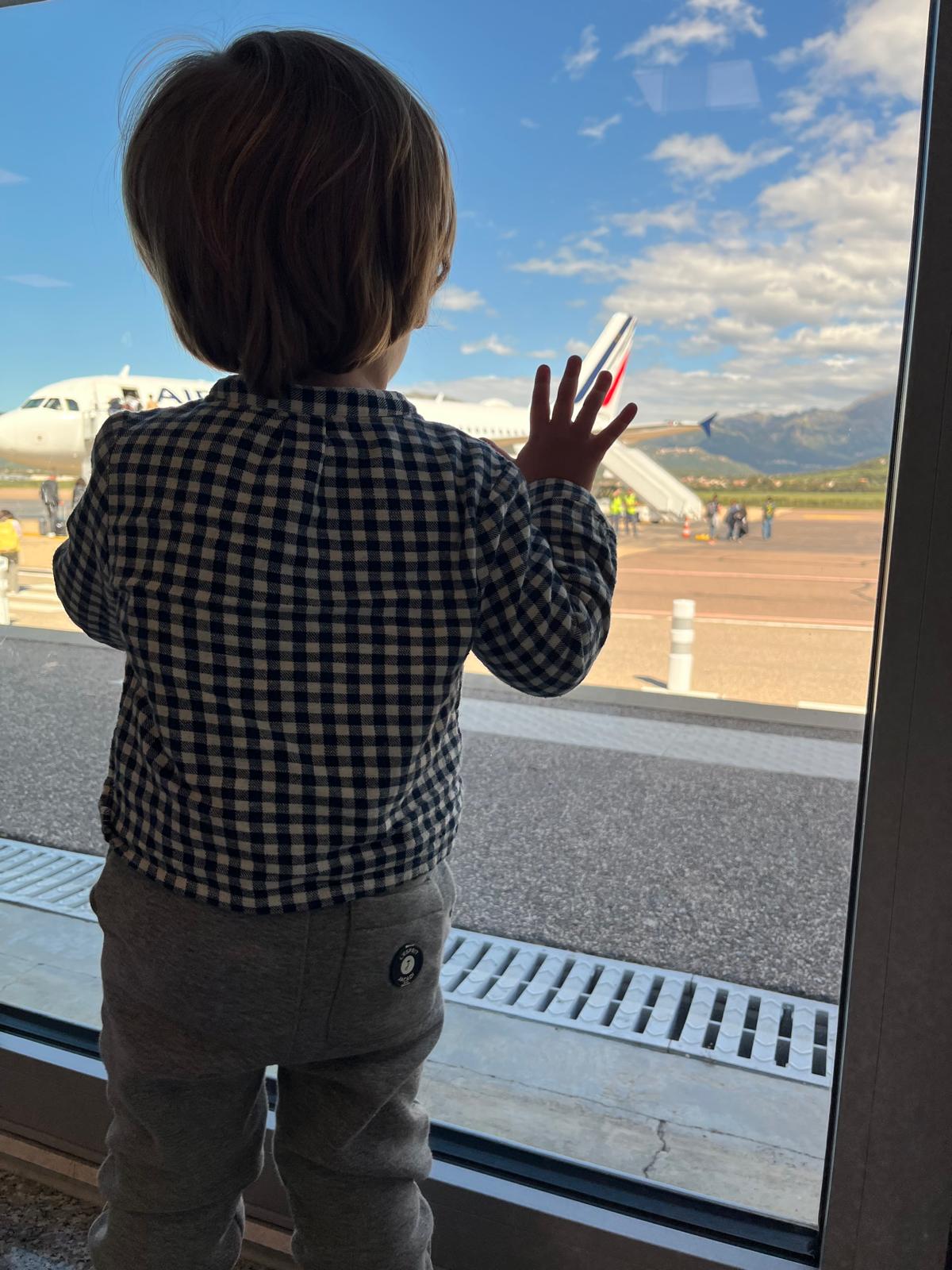 Enfant devant une vitre à l'aéroport qui regarde un avion